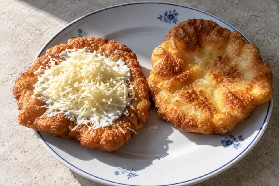 Kisebb, aranybarna gyors joghurtos lángos tejföllel és reszelt sajttal egy egyszerű tányéron